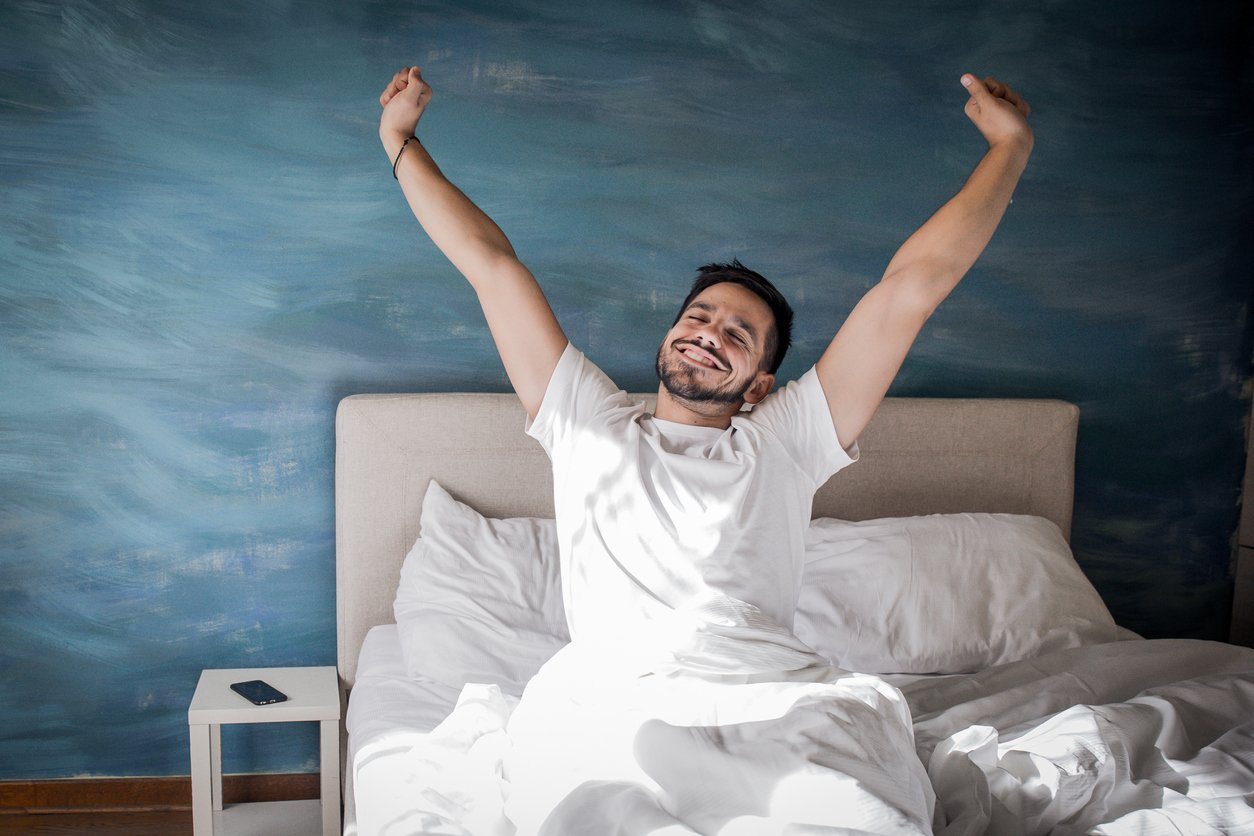 happy man stretching in bed in the morning