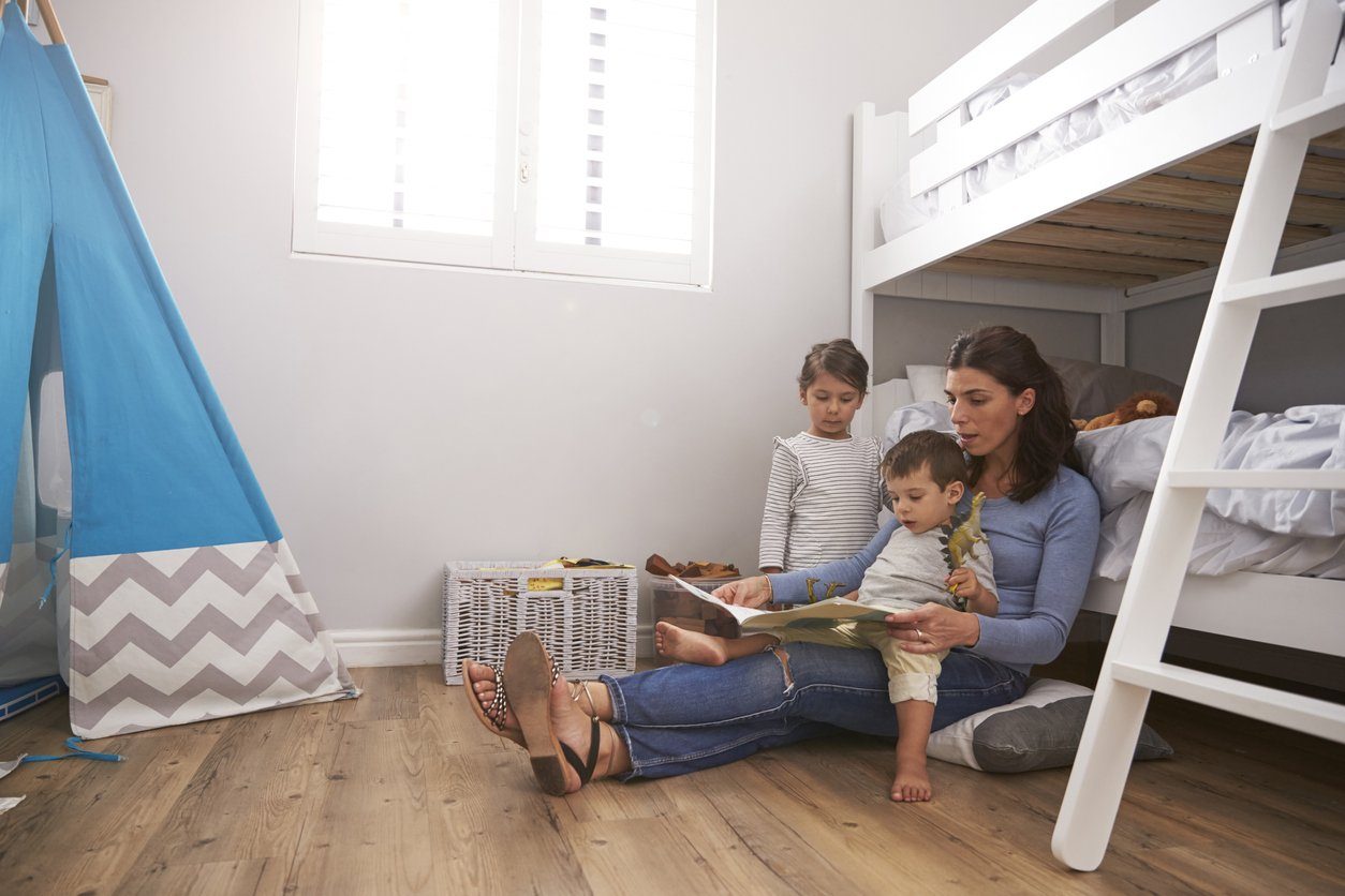 mother reading book to young children next to bunk beds