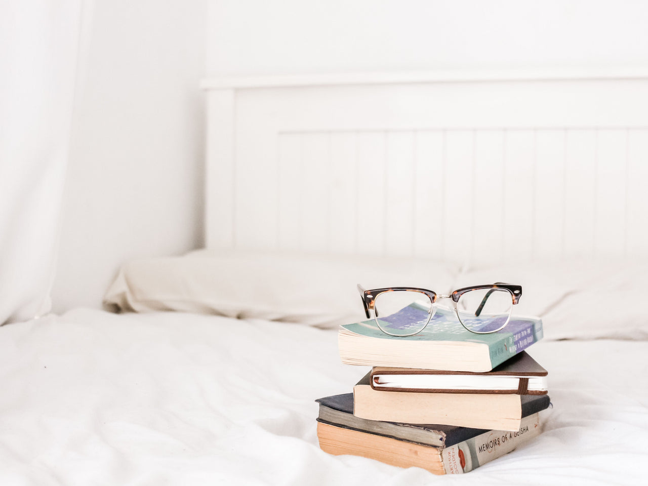 stack of books and eyeglasses on bed with perfect pillows