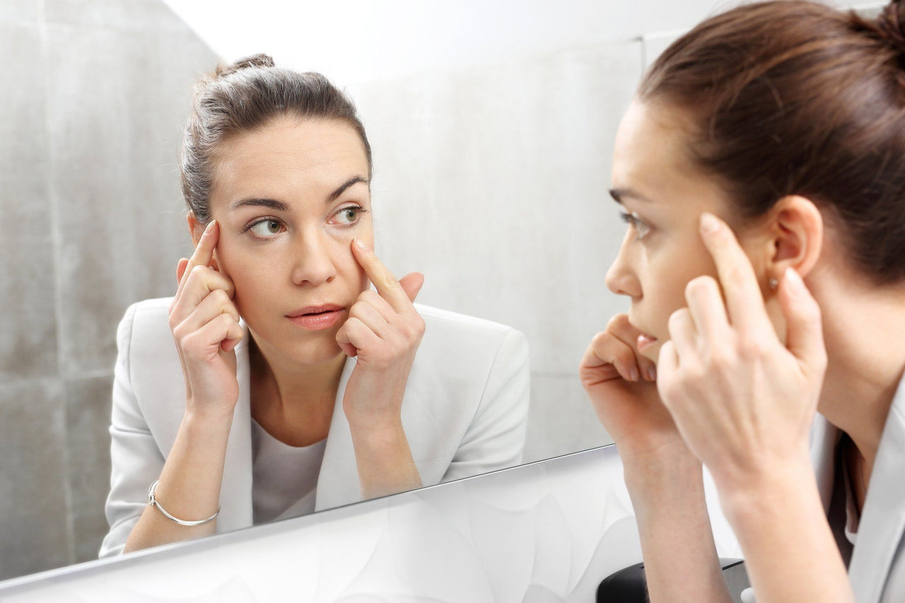 woman looking at eye wrinkles in mirror