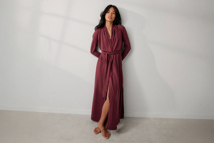 Woman wearing a burgundy long dress with a slit standing against a plain white background