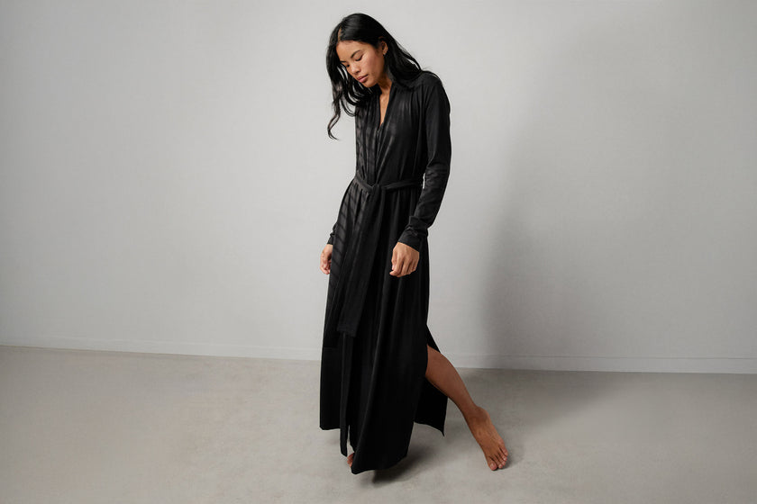 Woman wearing a black maxi robe with a side slit on a plain background
