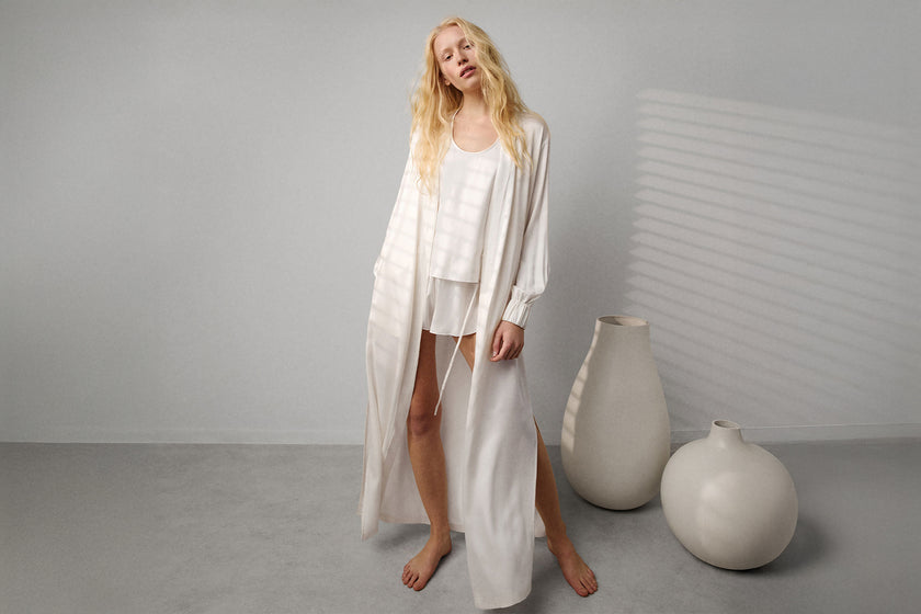 woman wearing white silk long robe and white pajamas against a white wall
