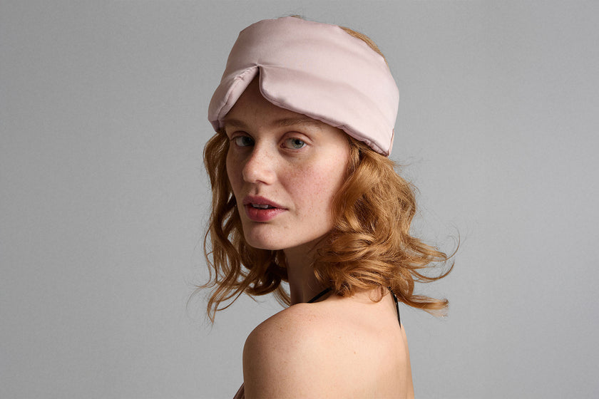 Woman wearing a pink sleep mask against a gray background