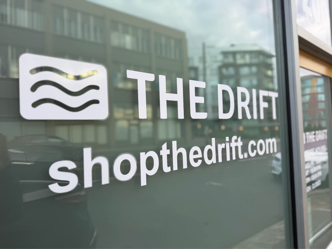 Glass storefront window with 'The Drift' logo and website text