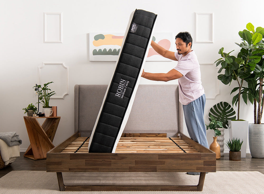 man pushing mattress on its side atop a bed frame