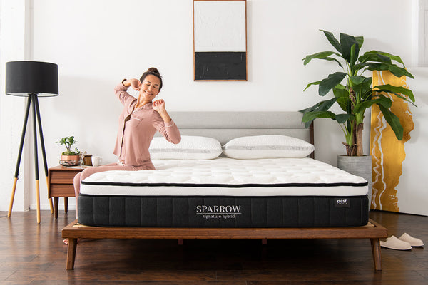 A woman peacefully waking up and stretching while sitting on the edge of her sparrow signature hybrid mattress 
