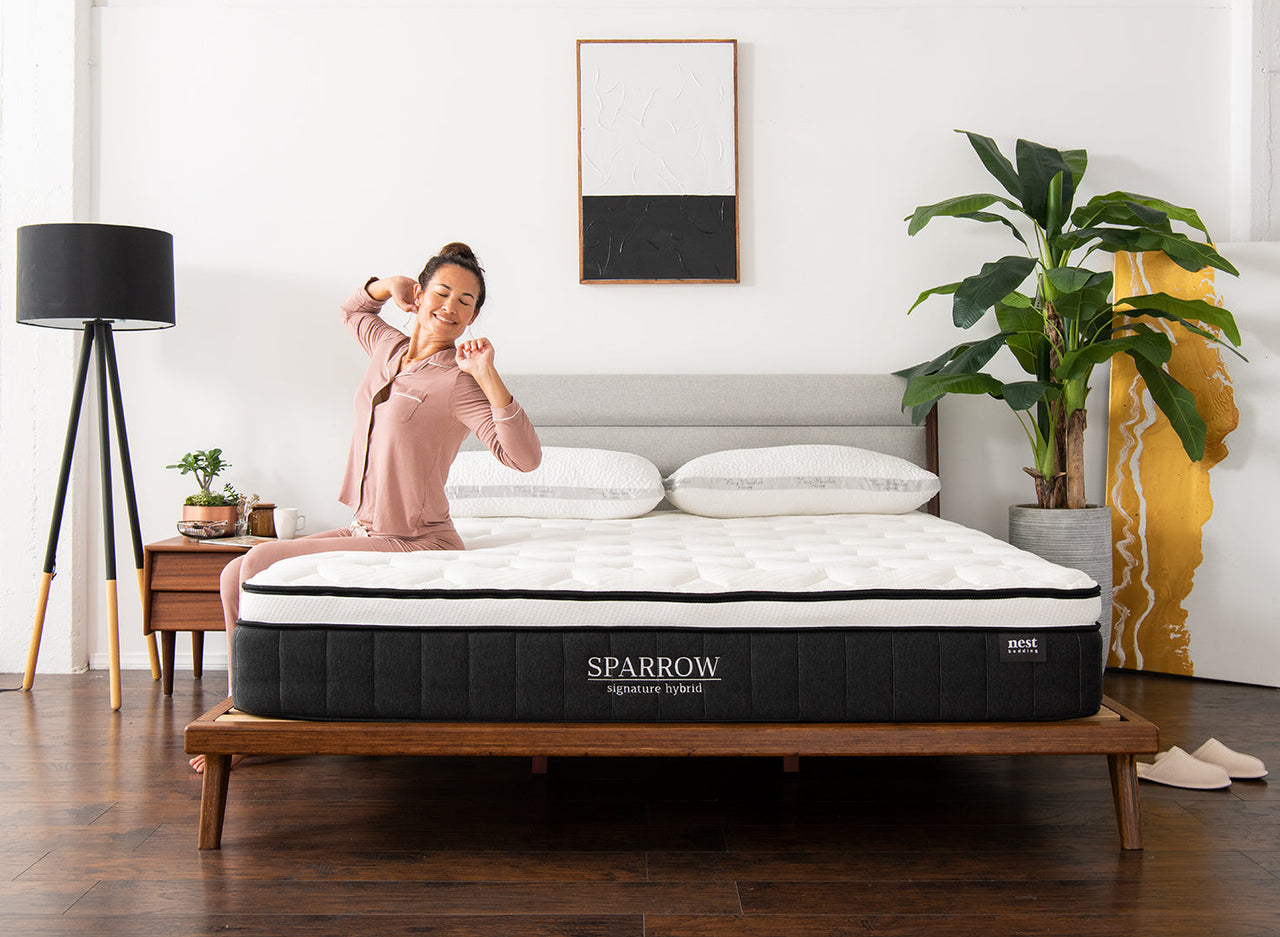 A woman peacefully waking up and stretching while sitting on the edge of her sparrow signature hybrid mattress 