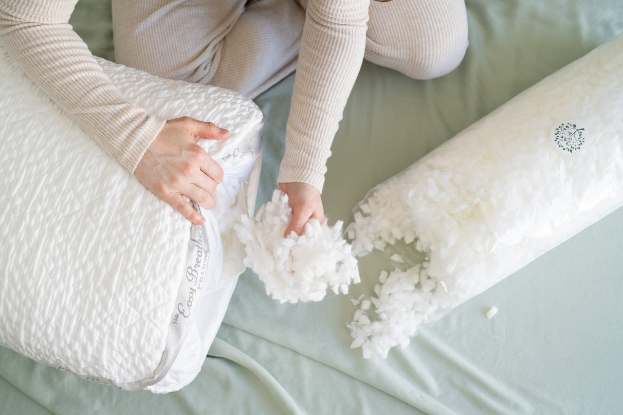 Person assembling a large white easy breather pillow on a bed by placing a handful of new shredded foam into the pillow