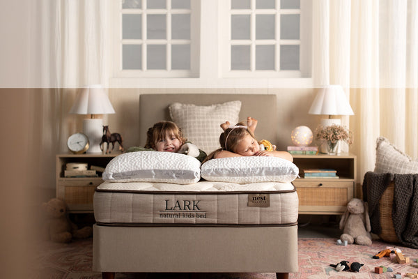 Two children lying on a Lark mattress in a bedroom with toys and furniture.