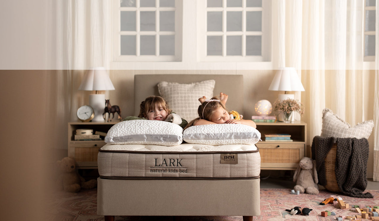 Two children lying on a Lark mattress in a bedroom with toys and furniture.