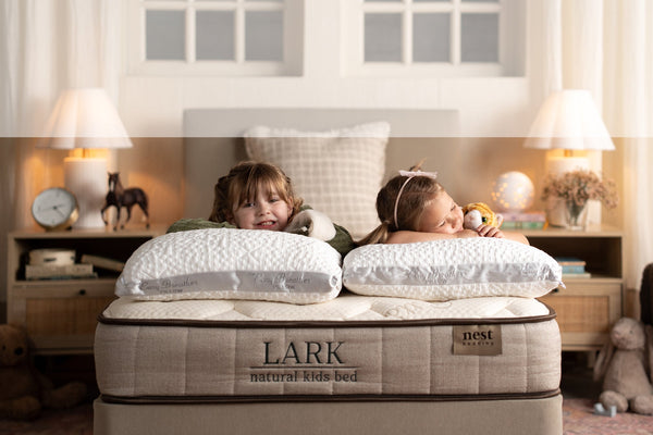 Two children lying on a Lark natural kids bed in a bedroom setting.