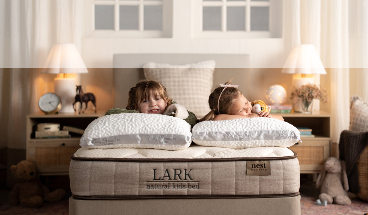 Two children lying on a Lark natural kids bed in a bedroom setting.