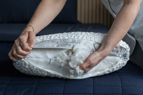 A woman's hands removing shredded foam fill from the inside of an easy breather jr. side sleeper pillow
