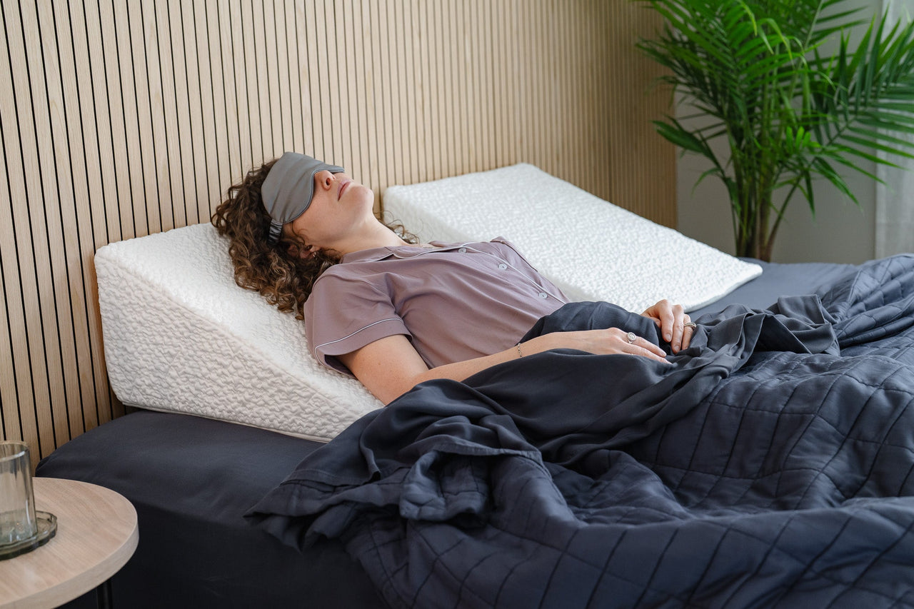 Woman lying on an easy breather wedge-shaped pillow in bed with a sleep mask on.