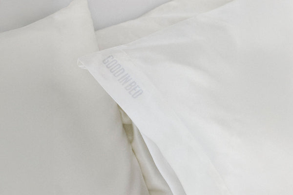 Close-up of a white pillow with 'Good In Bed' branding in a light gray background