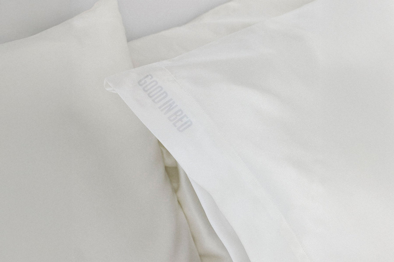 Close-up of a white pillow with 'Good In Bed' branding in a light gray background