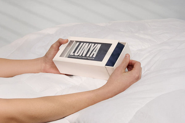 Person holding a box labeled 'LUNYA' on a bed