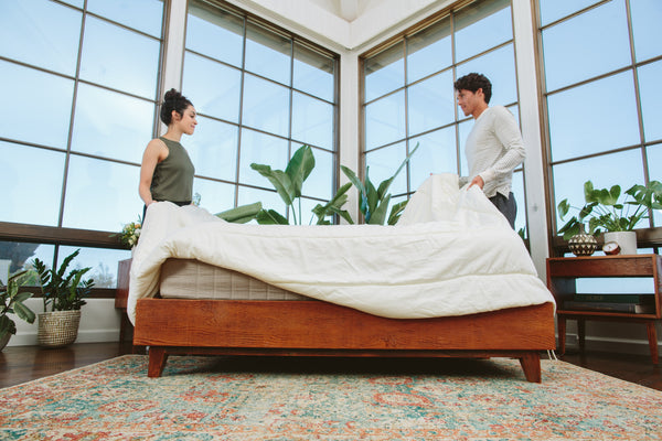 A couple making the bed with a comforter.