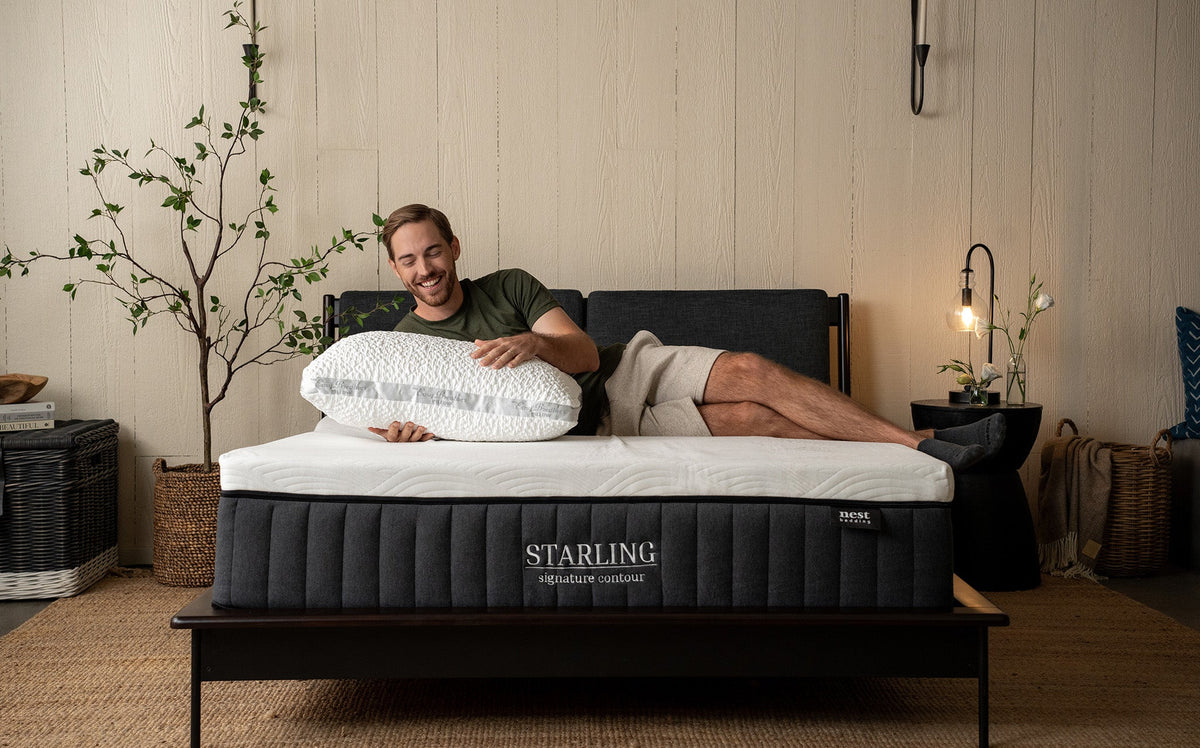 a man joyfully lying on his side while on a starling mattress and holding a plush easy breather pillow