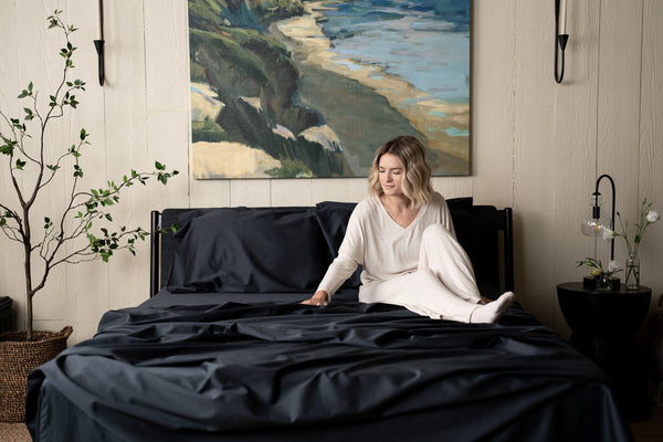 Slate Grey Sateen Organic Cotton Luxury Sheet Sets, woman sitting on bed feeling soft cotton sheets