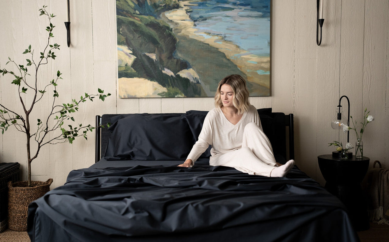 Slate Grey Sateen Organic Cotton Luxury Sheet Sets, woman sitting on bed feeling soft cotton sheets