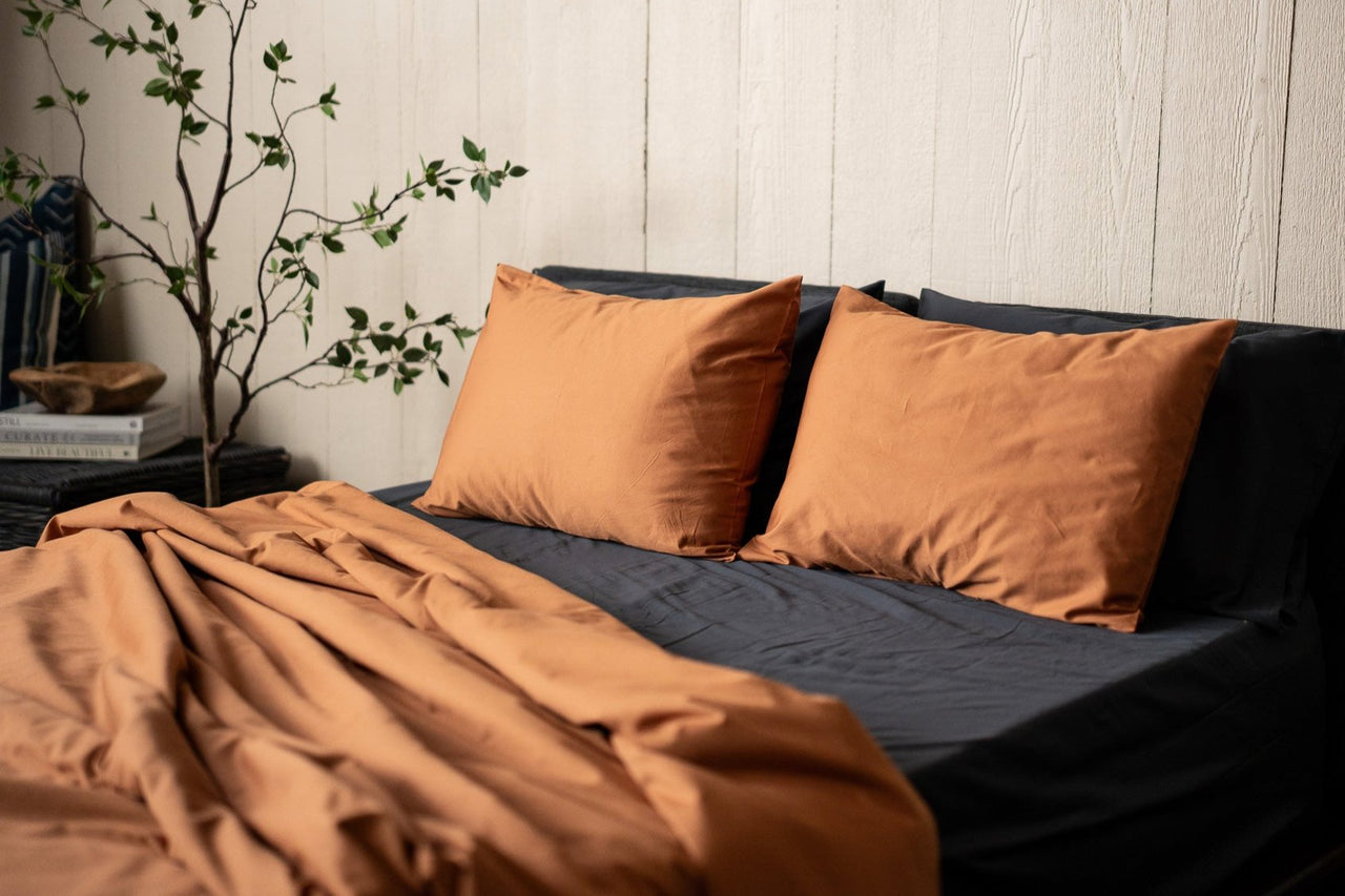 a fully made bed with shams and duvet cover, displayed in two different colors (terracotta and slate).  