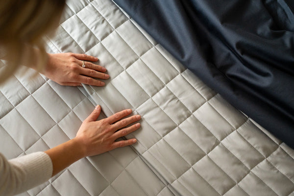 nest bedding, bamboo lightweight luxury quilt set, pewter, light grey, closeup rectangle stitch texture of quilt, woman's hands feeling soft fabric