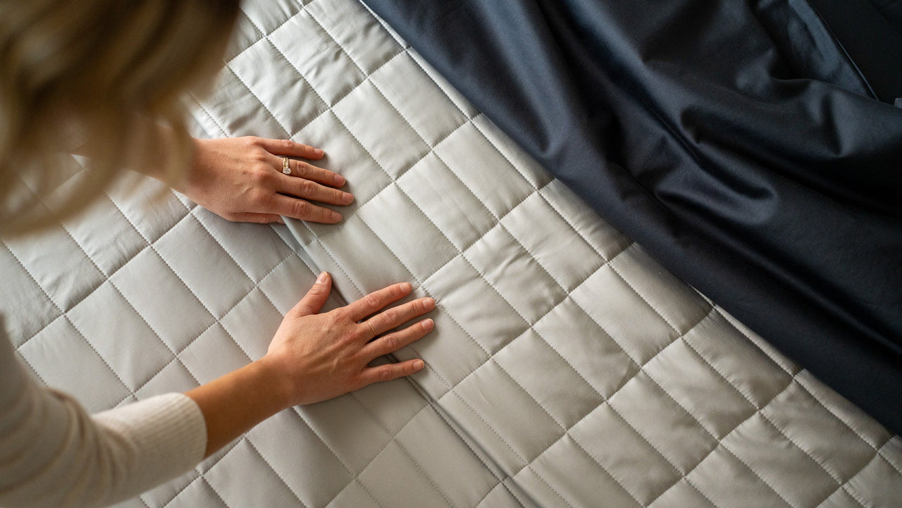 nest bedding, bamboo lightweight luxury quilt set, pewter, light grey, closeup rectangle stitch texture of quilt, woman's hands feeling soft fabric