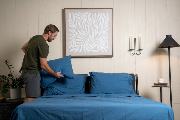 Man making the bed with blue sheets