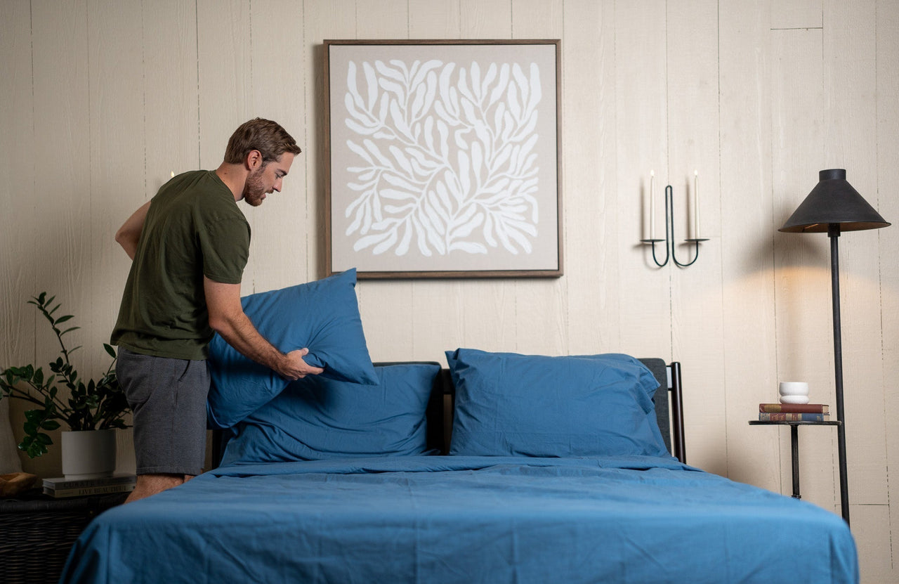 Man making the bed with blue sheets
