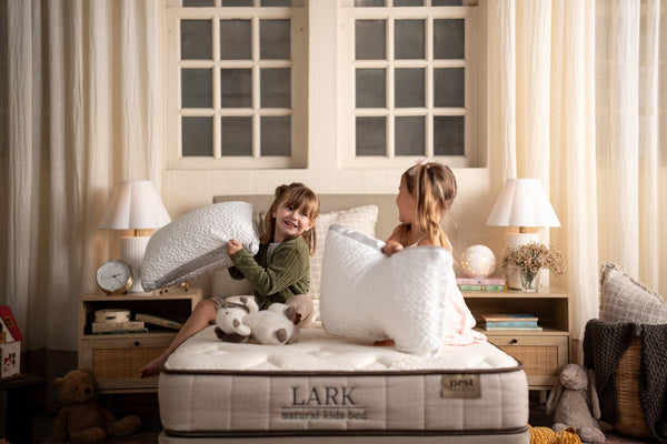 two young girls sitting on a lark natural kids bed having a pillow fight while each holding an easy breather jr. pillow