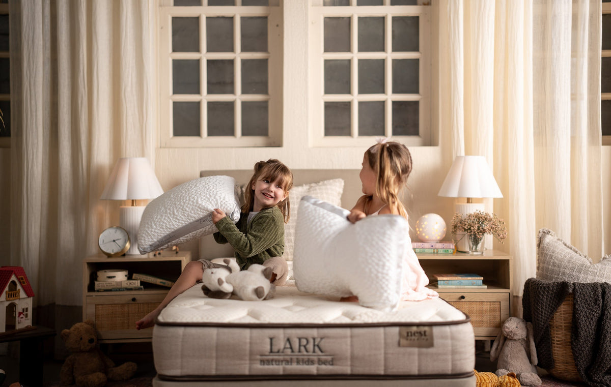 two young girls sitting on a lark natural kids bed having a pillow fight while each holding an easy breather jr. pillow