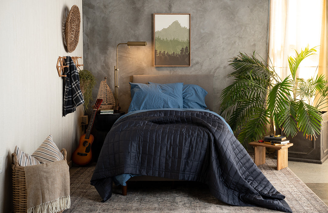 Cozy teen bedroom with a bed covered in a dark blue comforter, plants, and a guitar.