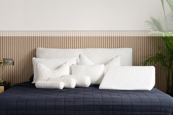 Bed with white pillows and a dark quilt against a wooden headboard.