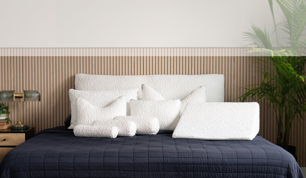 Bed with white pillows and a dark quilt against a wooden headboard.