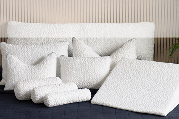 Set of white pillows on a bed with a wooden headboard.