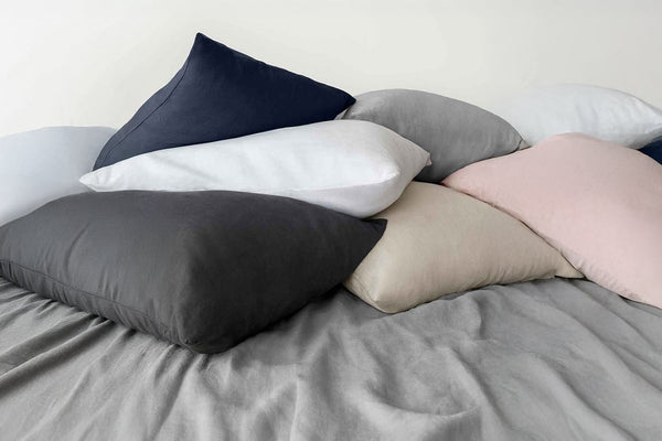 Collection of various colored of the linen pillows on a bed with a neutral background