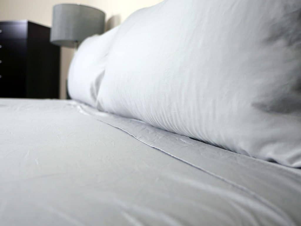 a closeup photo of light grey bamboo sheets on a bed