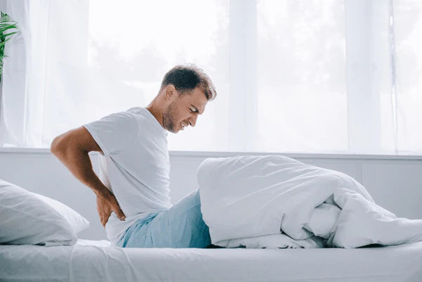 man sitting up in bed holding back in pain
