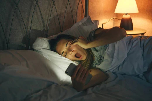 woman on her phone in bed while trying to fall asleep