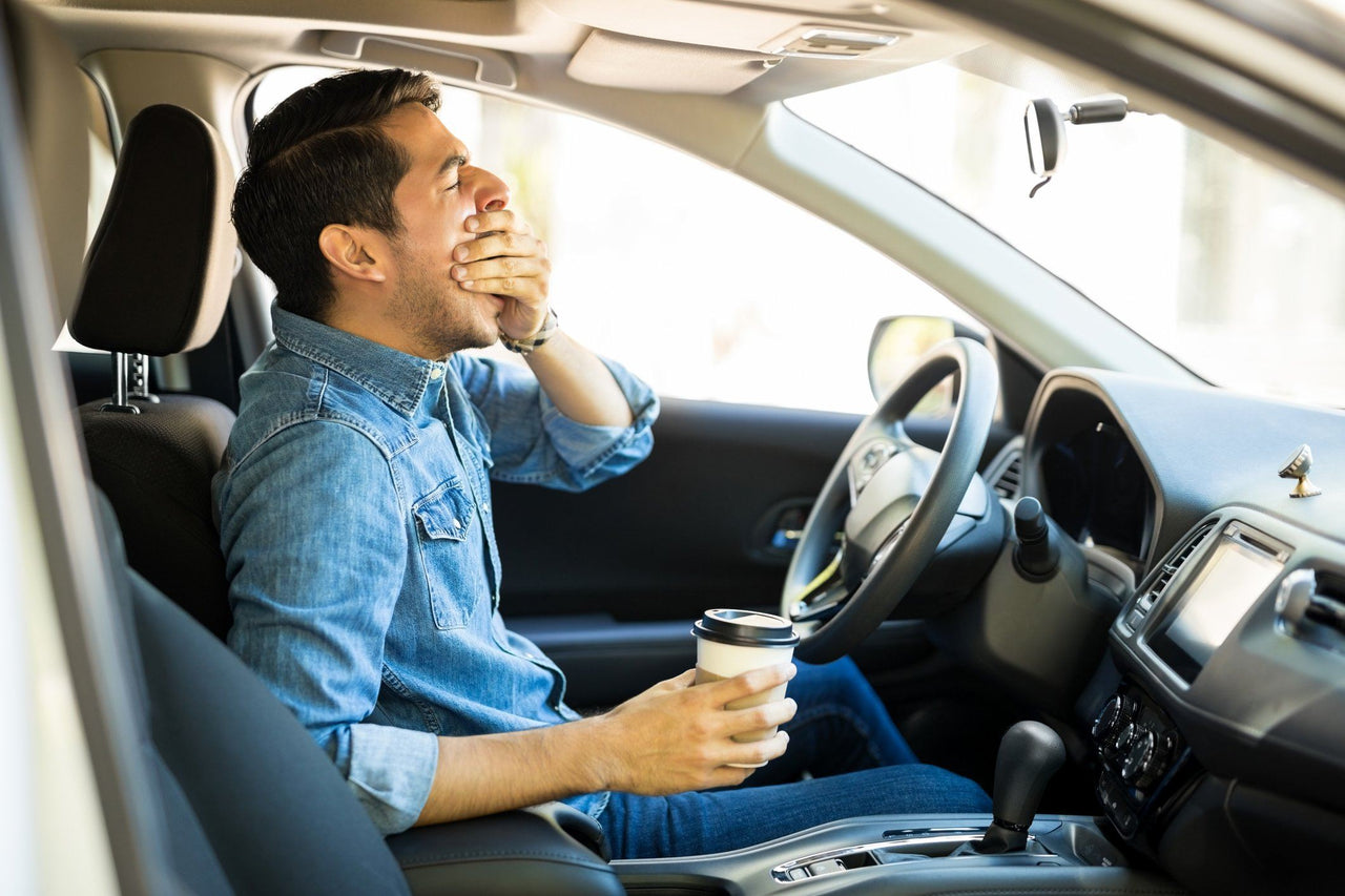 drowsy driver yawns at the wheel holding coffee after skimping on sleep