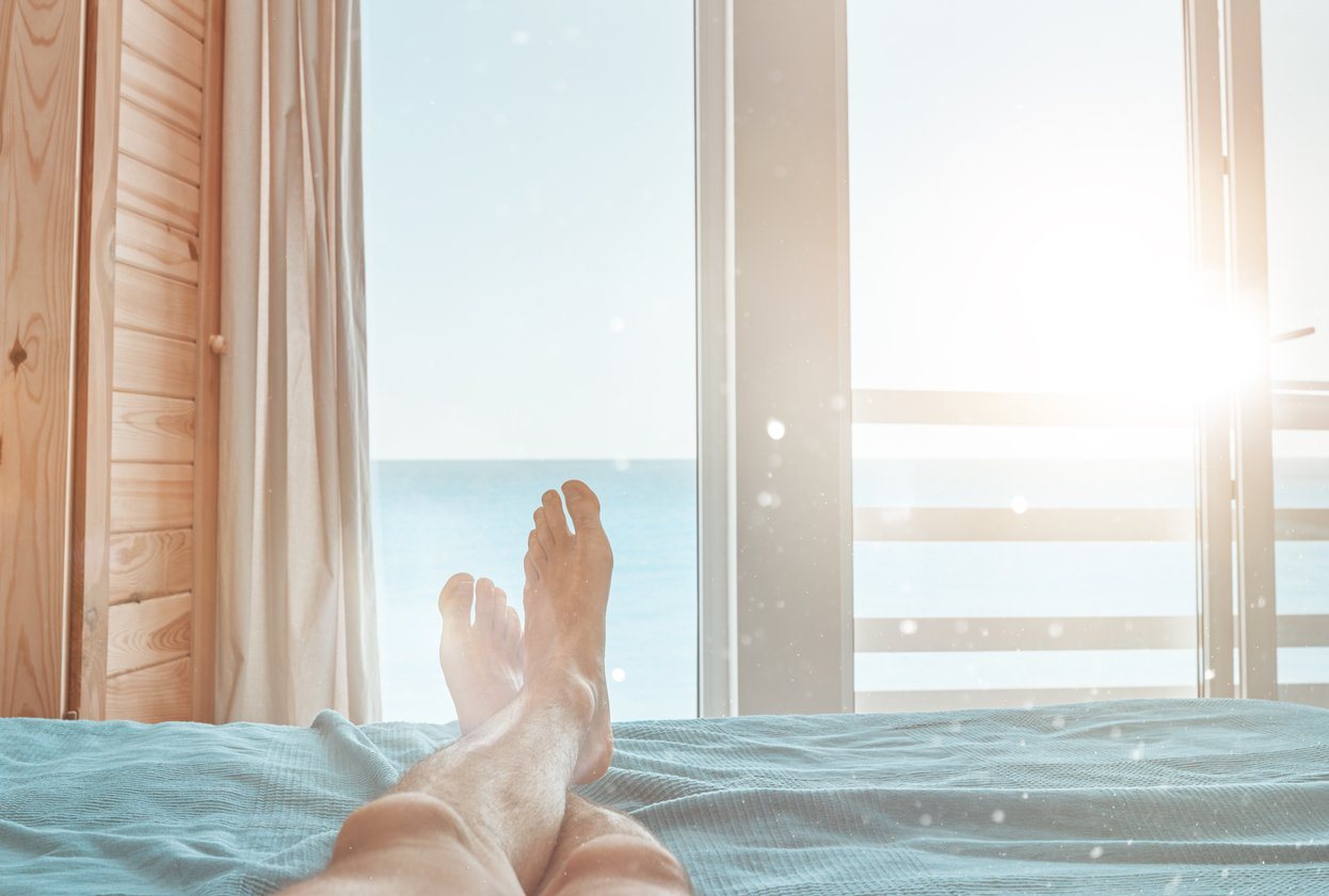 feet relaxed on a bed facing an ocean sunrise