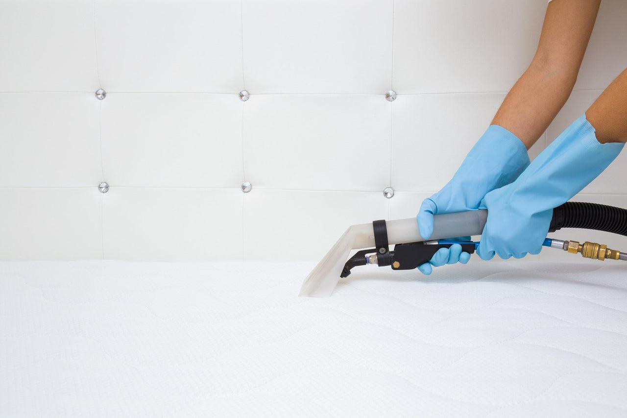gloved hands vacuuming mattress