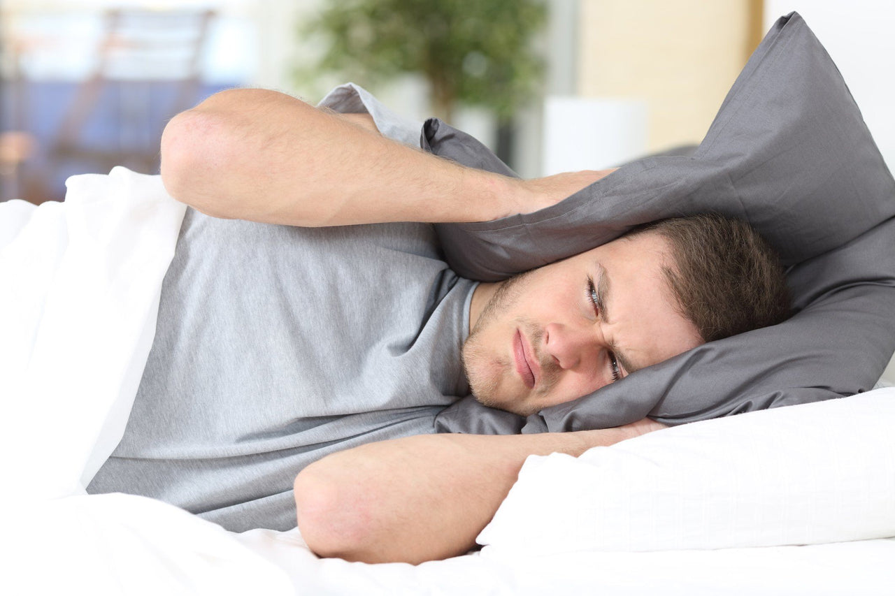 man covering ears with pillow for ambient noise