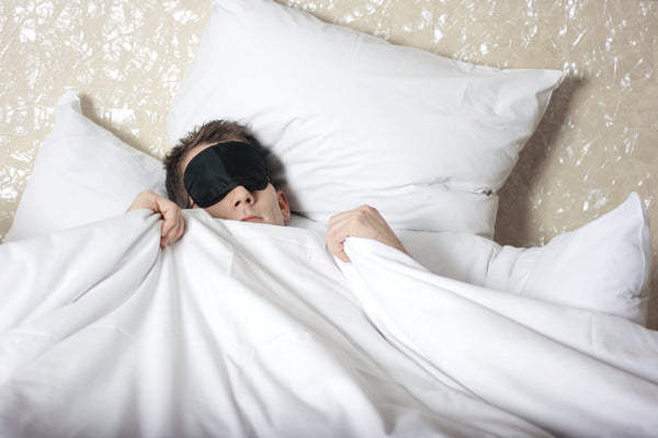man wearing sleep mask in bed for better sleep on a budget