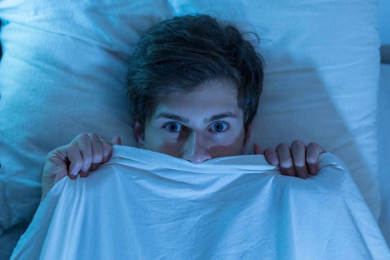 man wide awake under sheets with sleep paralysis