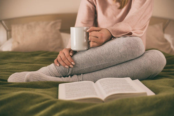 Woman drinking hot cup of tea in bed with book