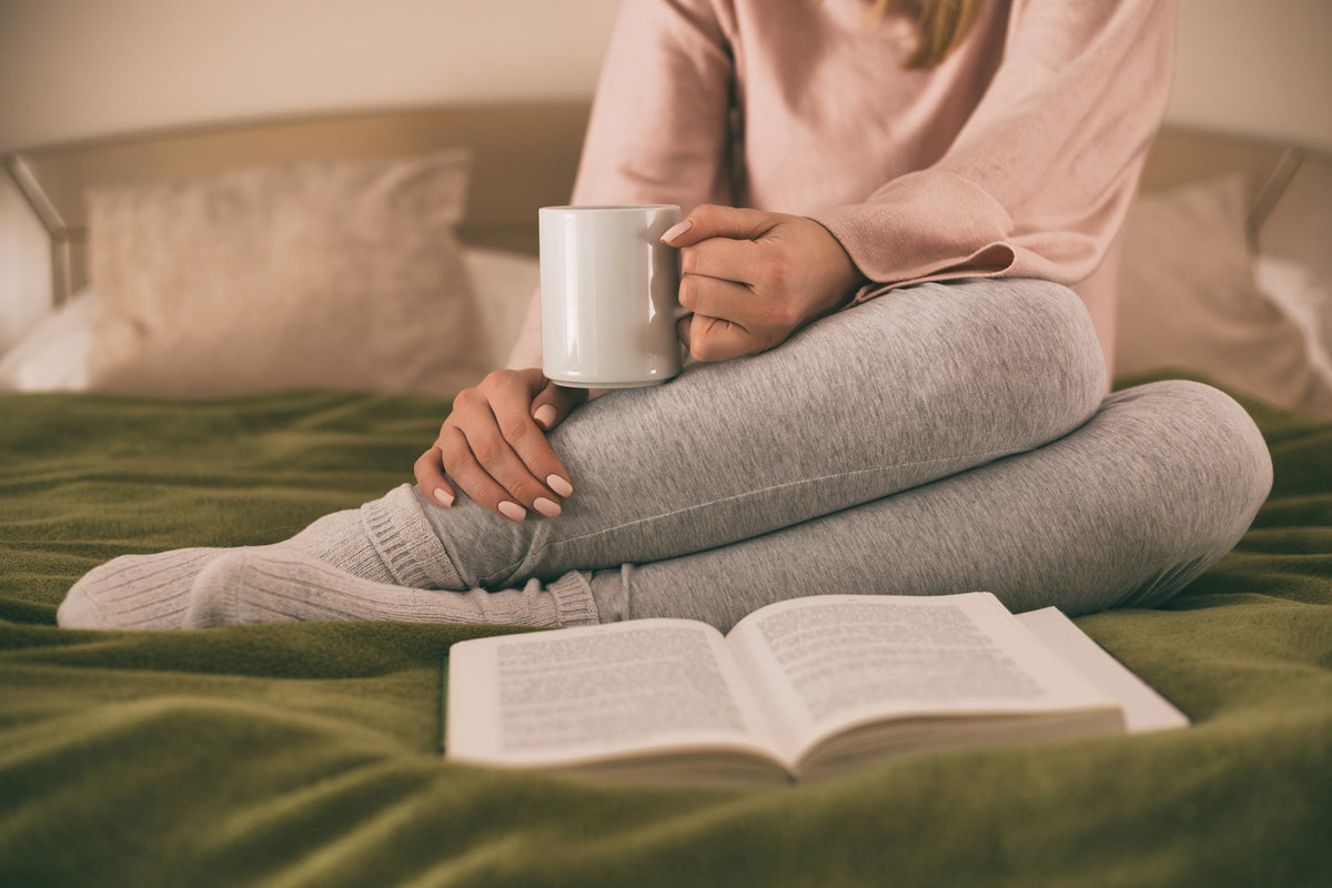 Woman drinking hot cup of tea in bed with book