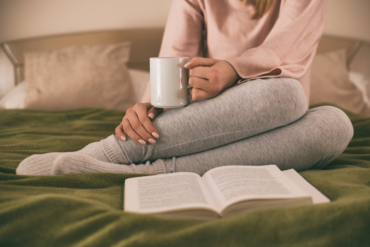 Woman drinking hot cup of tea in bed with book